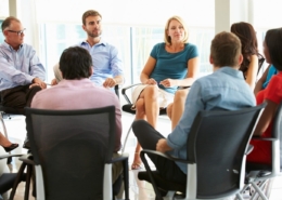 Business meeting with people sat on chairs in a circle.